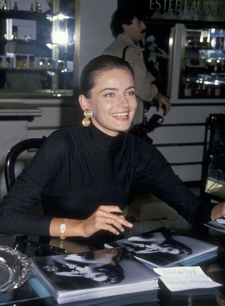 a woman sitting at a table in front of some books and smiling for the camera