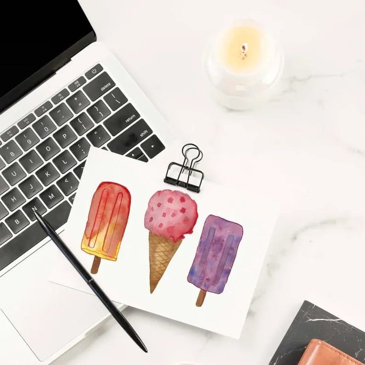 an open laptop computer sitting on top of a desk next to two ice cream cones