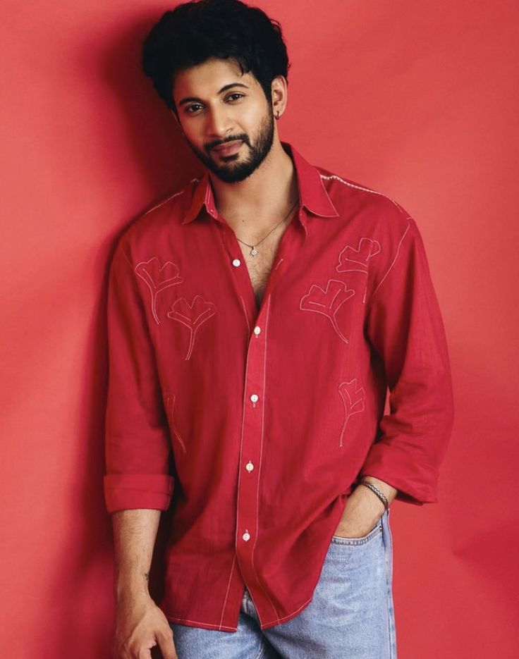 a man standing in front of a red wall with his hands on his hips and looking at the camera