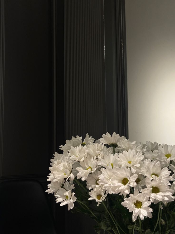 a vase filled with white daisies sitting on top of a table next to a mirror