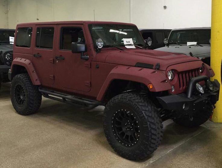 a red jeep parked in a garage next to other cars