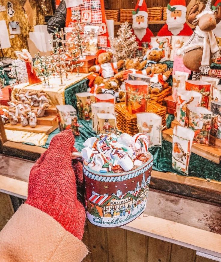 a person's hand holding a bucket full of candy in front of a christmas display