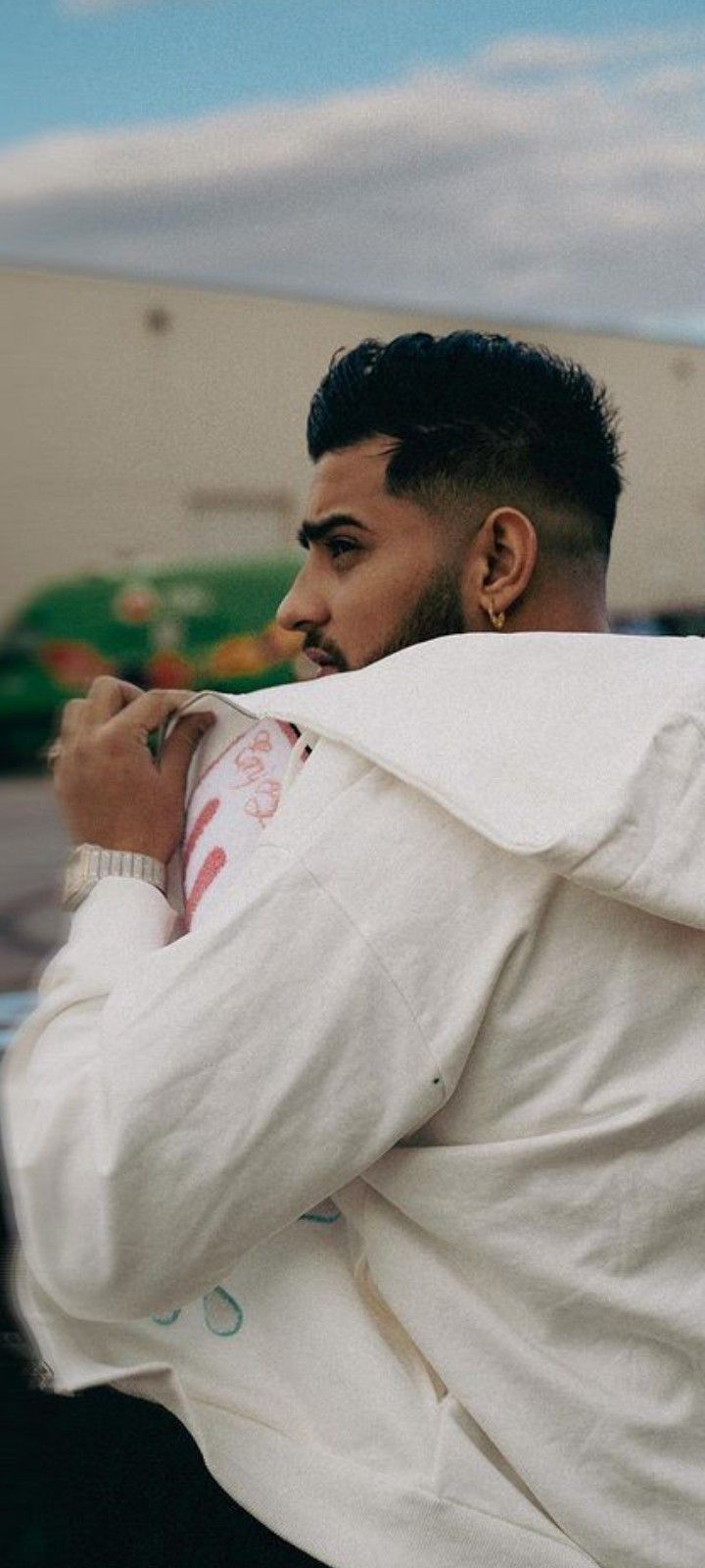 a man in a white jacket is leaning against a wall and looking off into the distance