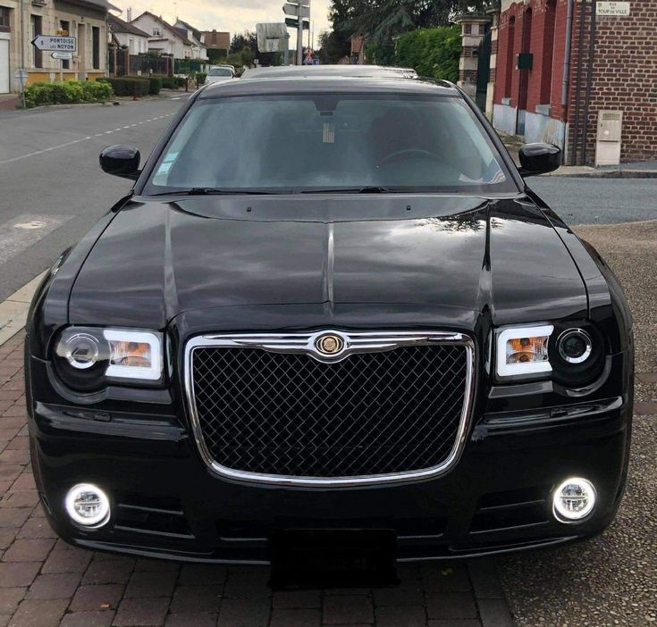 the front end of a black car parked on a brick sidewalk next to a street