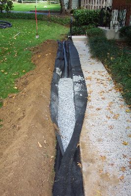 a large pipe laying on top of a dirt field next to a building and trees