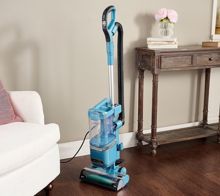 a blue vacuum is on the floor in front of a white couch and table with a pink pillow