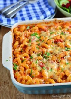 a casserole dish filled with pasta and vegetables on a wooden table next to a salad