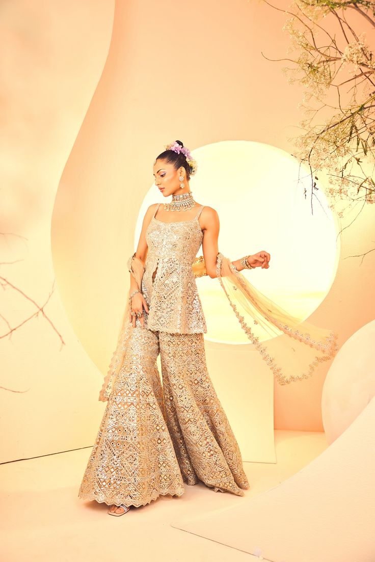 Showcasing a geometrical embroidered sharara and kurta with a dupatta. It is embroidered with gold foil and mirror embroidery. From Aneesh Agarwaal's Naksh collection. DELIVERY TIMEPlease allow 8-12 weeks for your outfit to arrive. FABRIC DETAILSTulle Professional cleaning only. Gold Palazzo Set With Intricate Embroidery And Straight Kurta, Gold Chanderi Palazzo Set With Intricate Embroidery, Reception Sharara With Straight Kurta And Zari Work, Designer Bollywood Sharara With Resham Embroidery, Festive Sharara With Mirror Work, Designer Sharara With Intricate Embroidery And Straight Kurta, Bollywood Style Chinon Sharara For Reception, Gold Sharara With Intricate Embroidery For Eid, Designer Palazzo Set With Intricate Embroidery For Eid