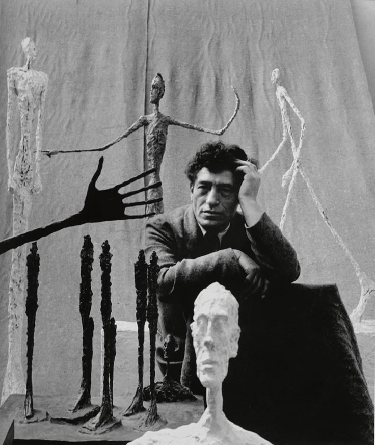 a black and white photo of a man sitting in front of a sculpture with his hands on his head