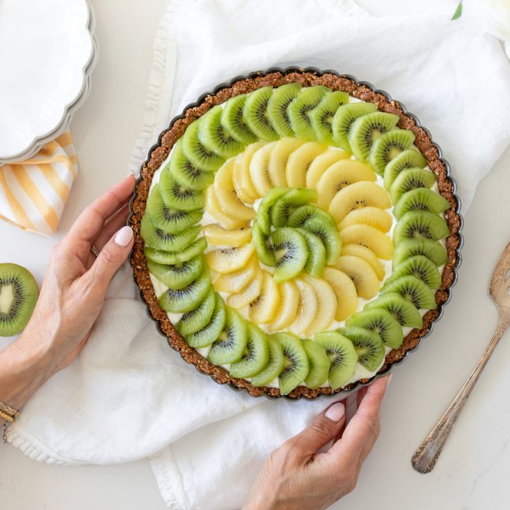 a person holding a pie with kiwi slices in it on top of a table