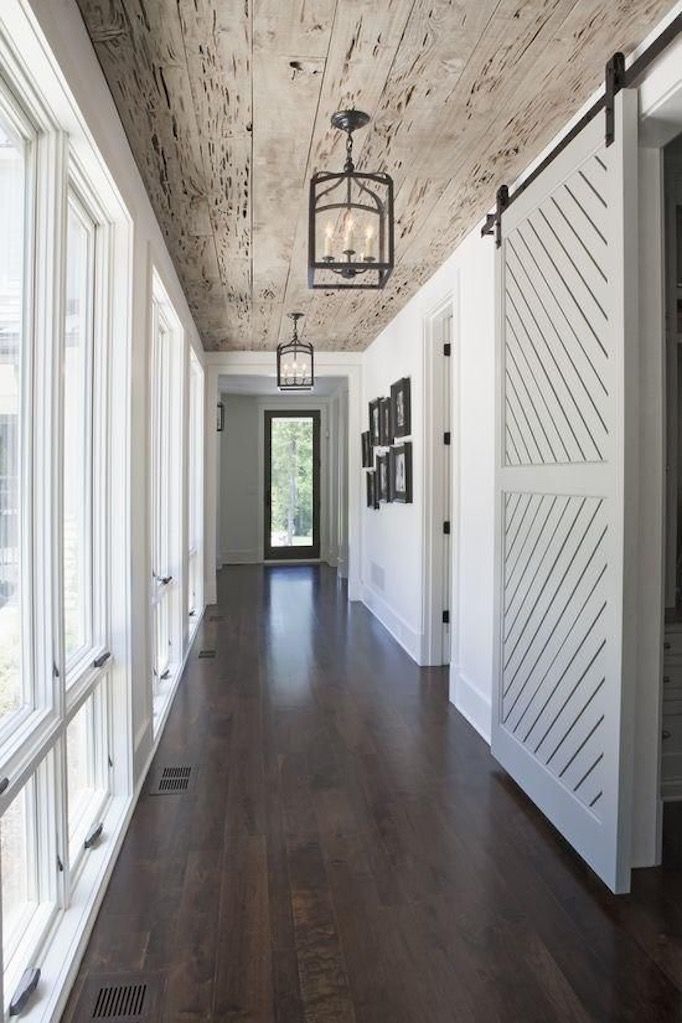 a long hallway with white walls and wood flooring is lit by an old fashioned light fixture