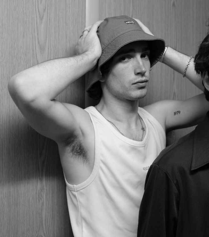 a man with a hat on his head standing next to another man wearing a tank top