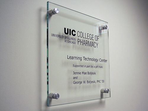 a clear glass plaque mounted to the side of a white wall that says ucc college of pharmacy