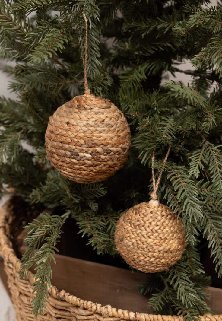 two christmas ornaments hanging from the top of a pine tree in a wicker basket