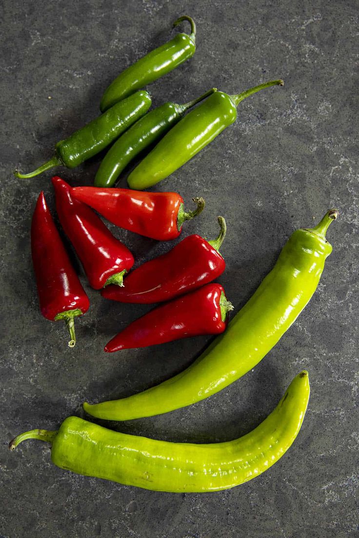 several green and red peppers on a gray surface with one pepper still attached to it