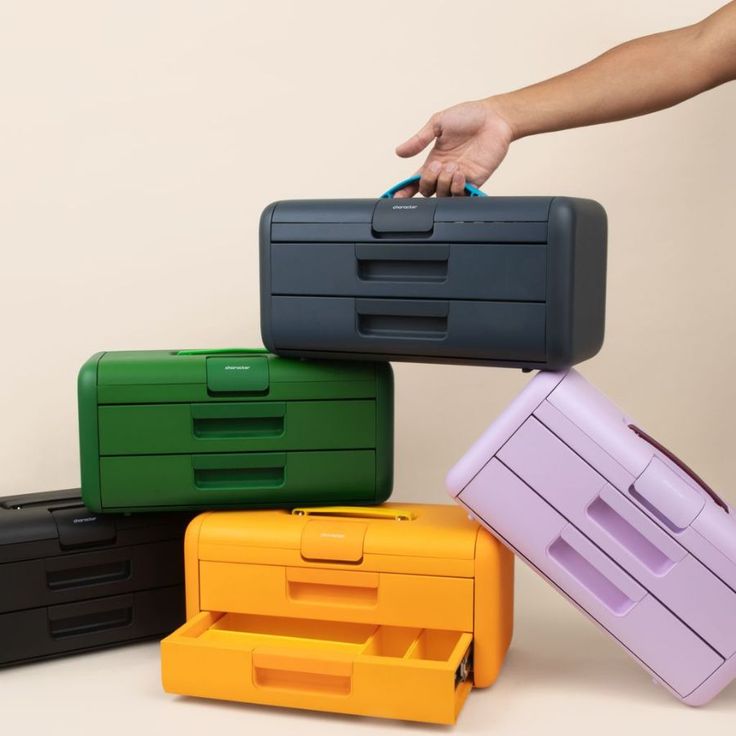 four different colored suitcases stacked on top of each other with one person's hand reaching for them