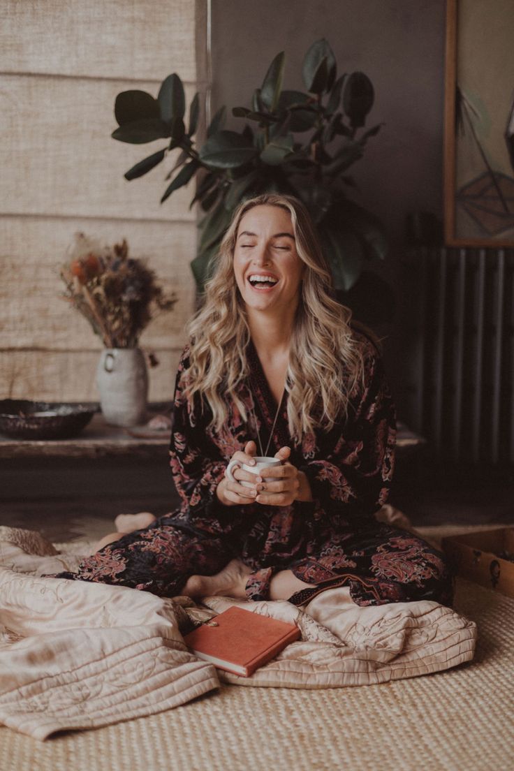 a woman sitting on the floor laughing and holding a cup in her hands while looking up