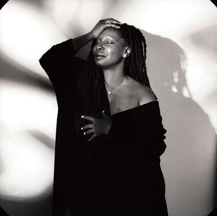 a black and white photo of a woman with her hands on her head, leaning against a wall