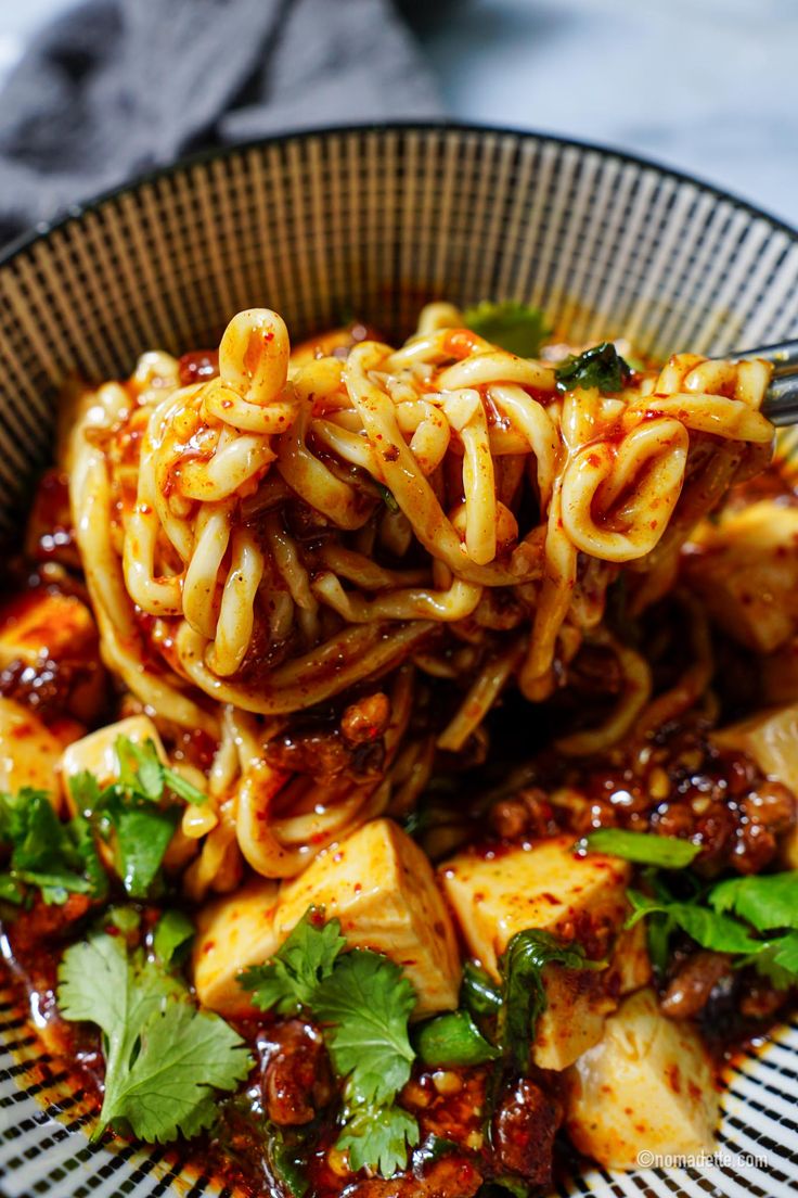 a bowl filled with noodles and sauce on top of a table next to a fork