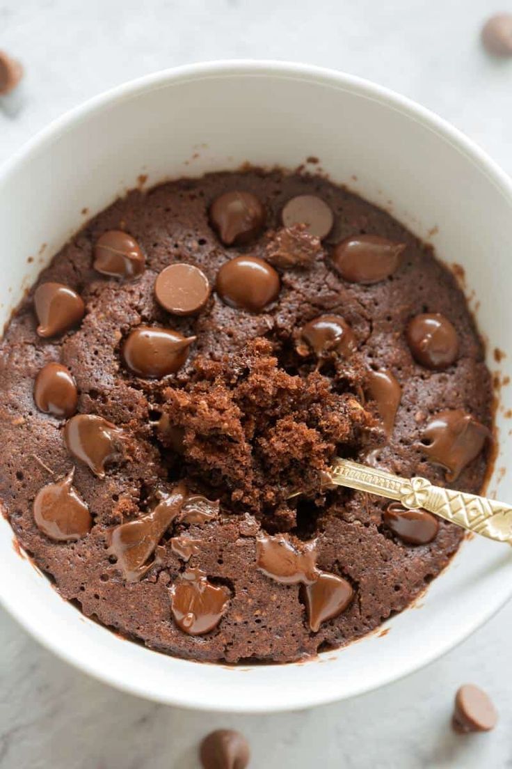 a white bowl filled with chocolate pudding and topped with a gold spoon, on top of a marble surface