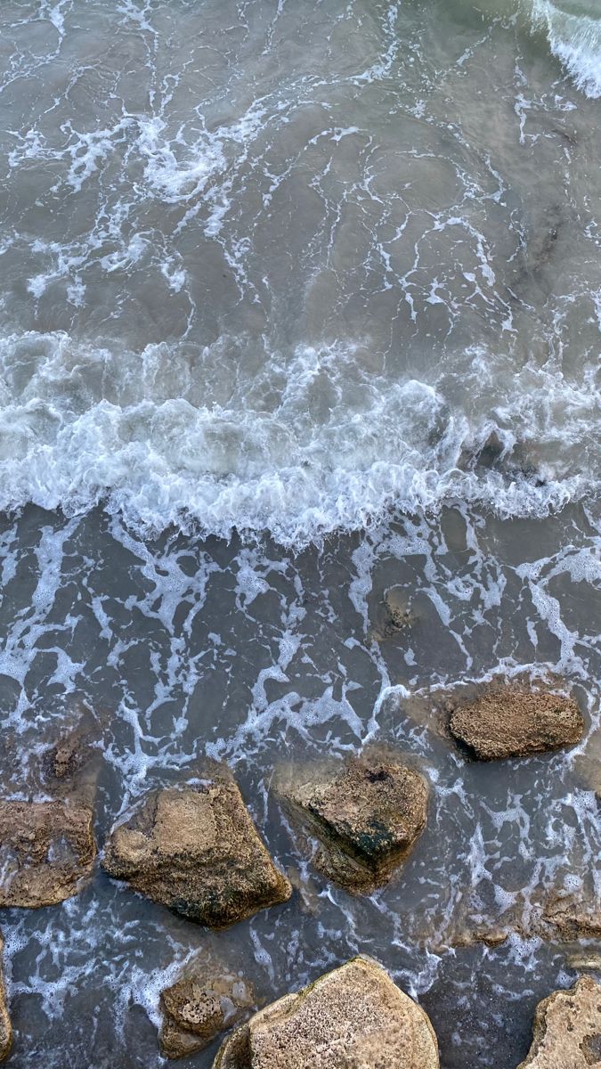 some rocks in the water and an umbrella on top of them by the beach shore