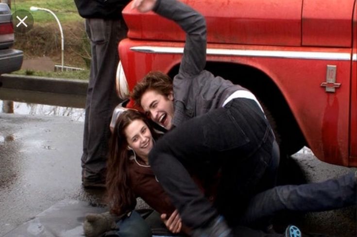 two people are sitting on the ground in front of a red truck