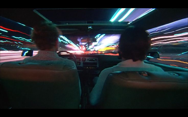 two people in the back seat of a car driving down a street at night time