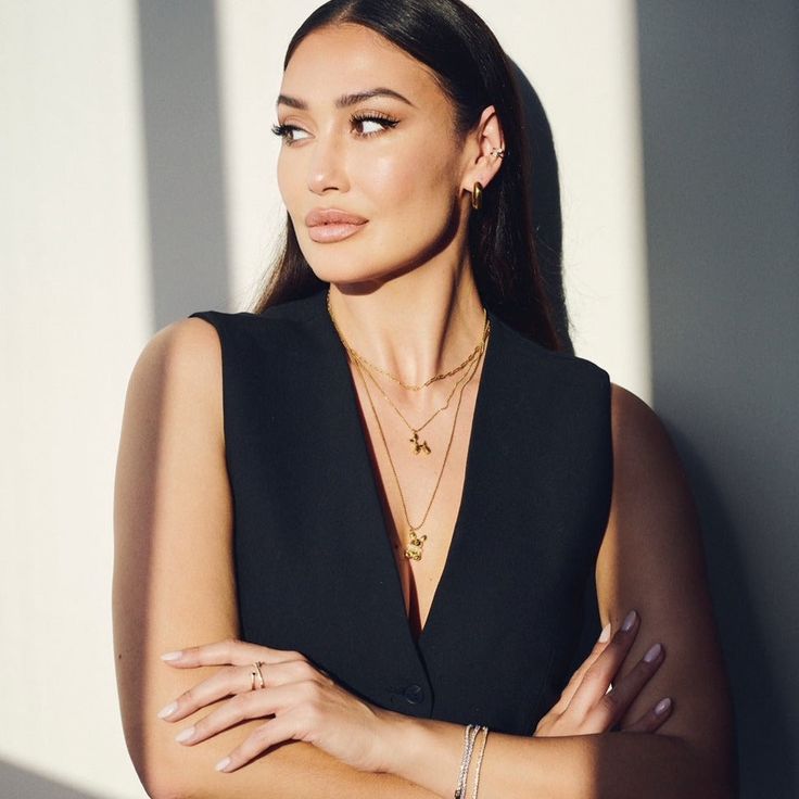 a woman with her arms crossed standing in front of a wall wearing a black dress