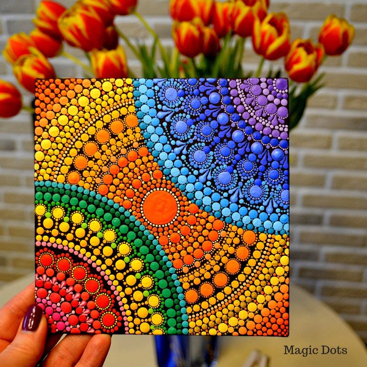 a hand holding up a colorful card with flowers in the background and a vase full of tulips behind it