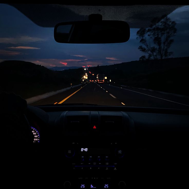 the dashboard of a car at night with lights on and dark clouds in the background