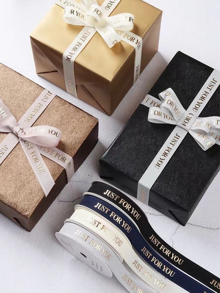 three wrapped gift boxes with ribbons and bows on them, one is black, the other is gold