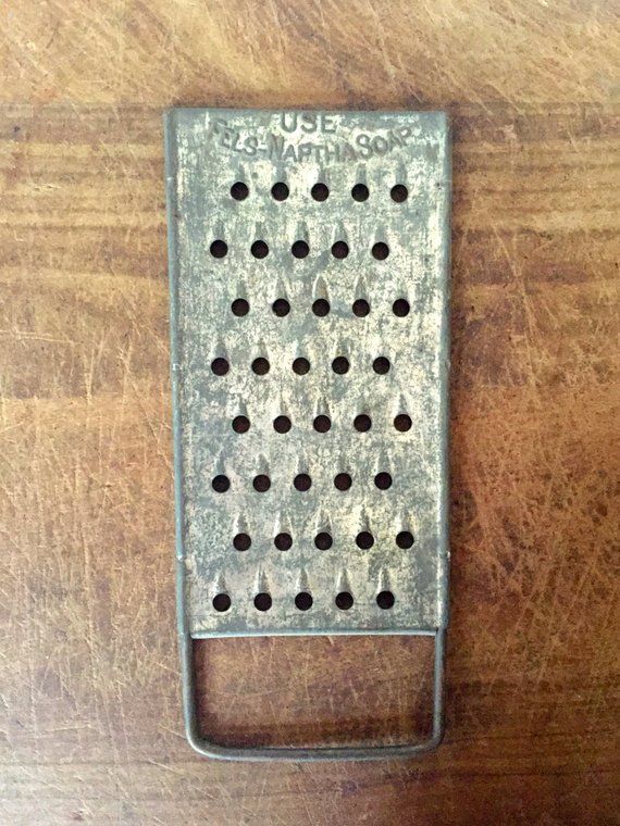 an old metal grater sitting on top of a wooden table with holes in it