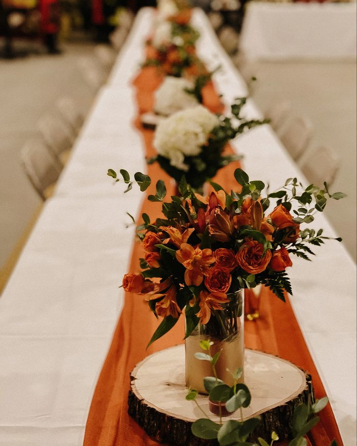 the long table is decorated with orange and white flowers in vases on wood slices