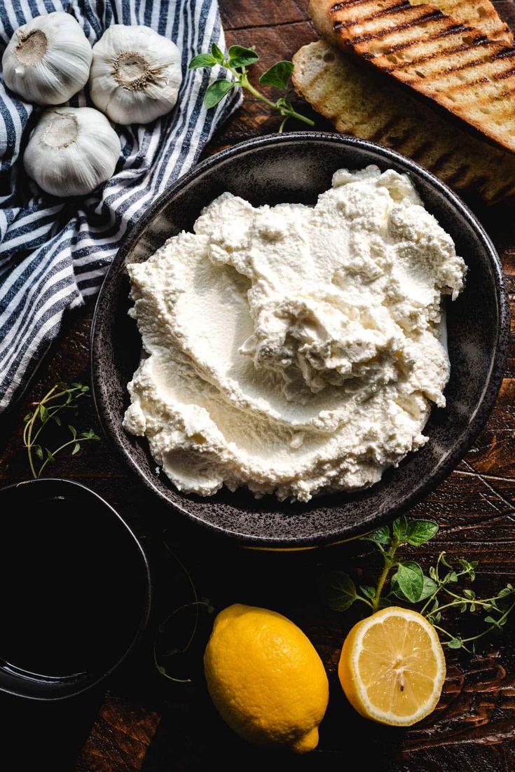 a bowl filled with cottage cheese next to sliced lemons and garlic on a wooden table