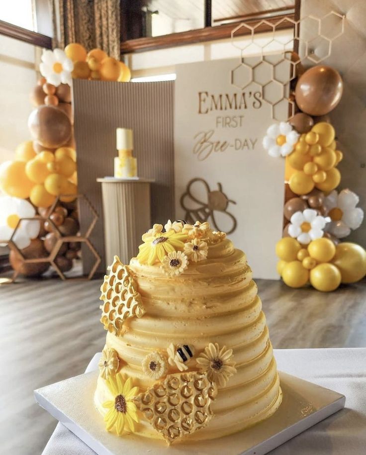 a three tiered cake sitting on top of a table next to balloons and honeycombs