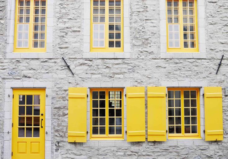 yellow windows on the side of a gray brick building with shutters open and closed