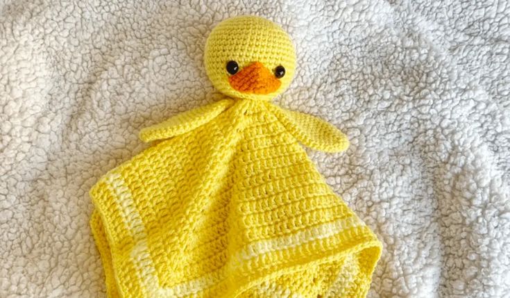 a crocheted yellow duck wrapped in a blanket on a white bedding sheet