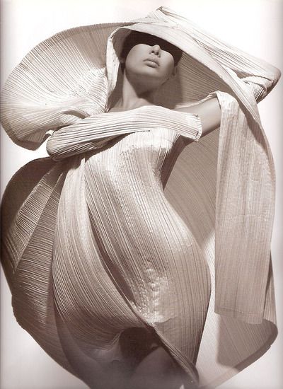 a mannequin wearing a large hat and flowing fabric around its head, in front of a white background