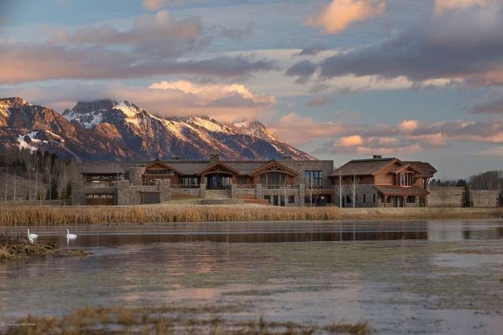 a large house sitting on the side of a lake next to a mountain covered in snow