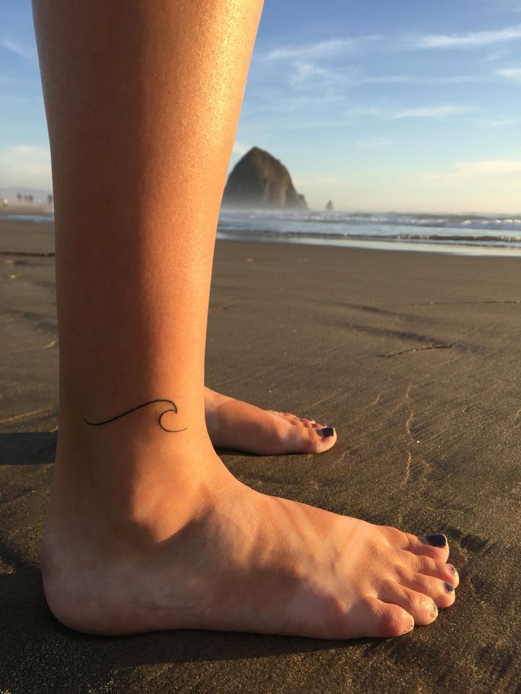 a woman's foot with a small wave tattoo on her left ankle and the ocean in the background