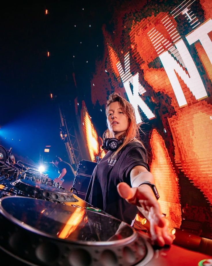 a woman dj mixing in front of a large screen with her hands out to the side