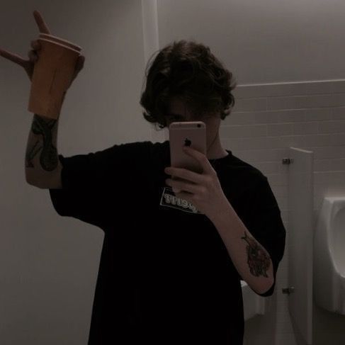 a man taking a selfie in the bathroom with his cell phone and cup on his arm