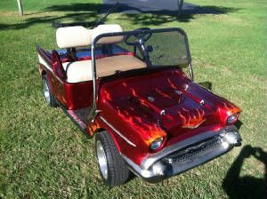 an old fashioned golf cart with flames on the front and back wheels, parked in grass