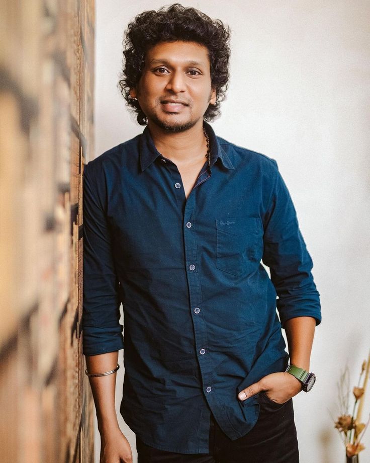 a man standing in front of a wooden door with his hand on his hip and looking at the camera