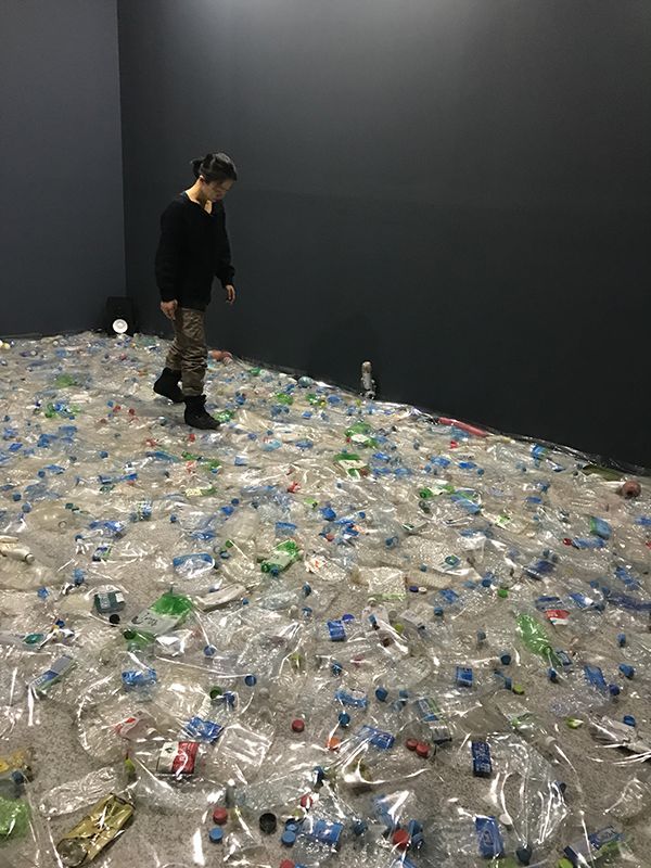 a man standing on top of a pile of plastic bottles in a room filled with trash