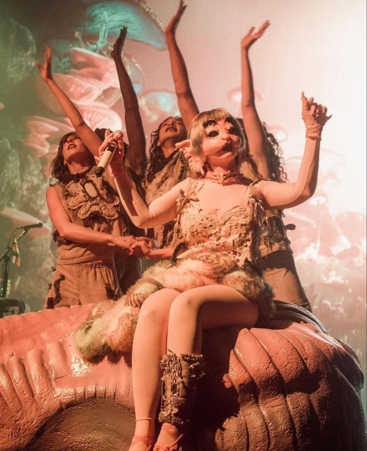 three women are sitting on an elephant with their arms in the air while one woman holds her leg up