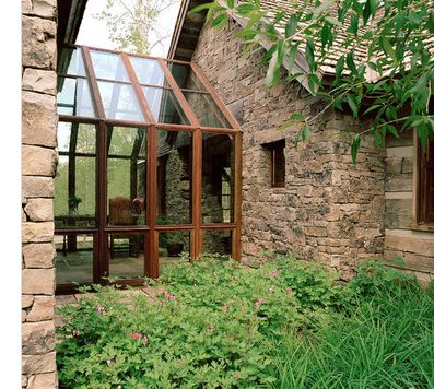 an old stone house is surrounded by greenery and flowers in the foreground, with large windows to let in light