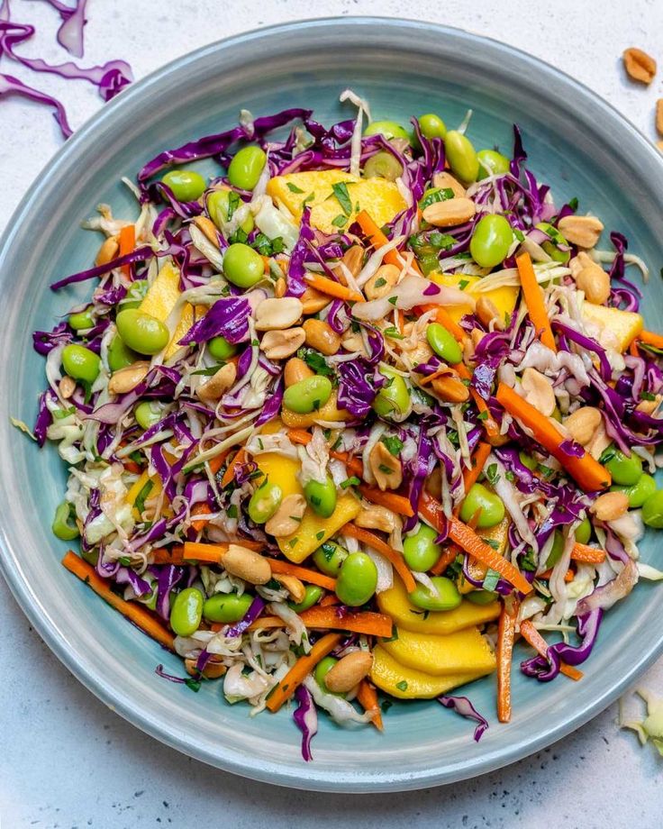 a salad with carrots, peas and cabbage in a bowl on a white table