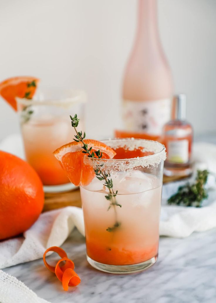 two glasses filled with orange margaritas and garnished with rosemary on the rim