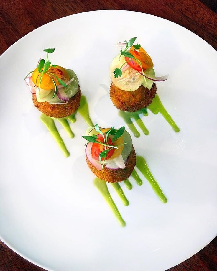 three small appetizers are on a white plate with green garnishes